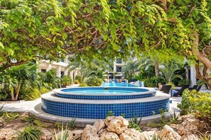 Una piscina circular con mosaicos azules, rodeada de sillas de descanso y palmeras.