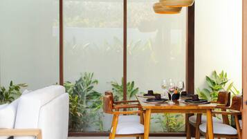 Un comedor con una mesa lista para dos personas, sillas de madera y un sofá blanco.