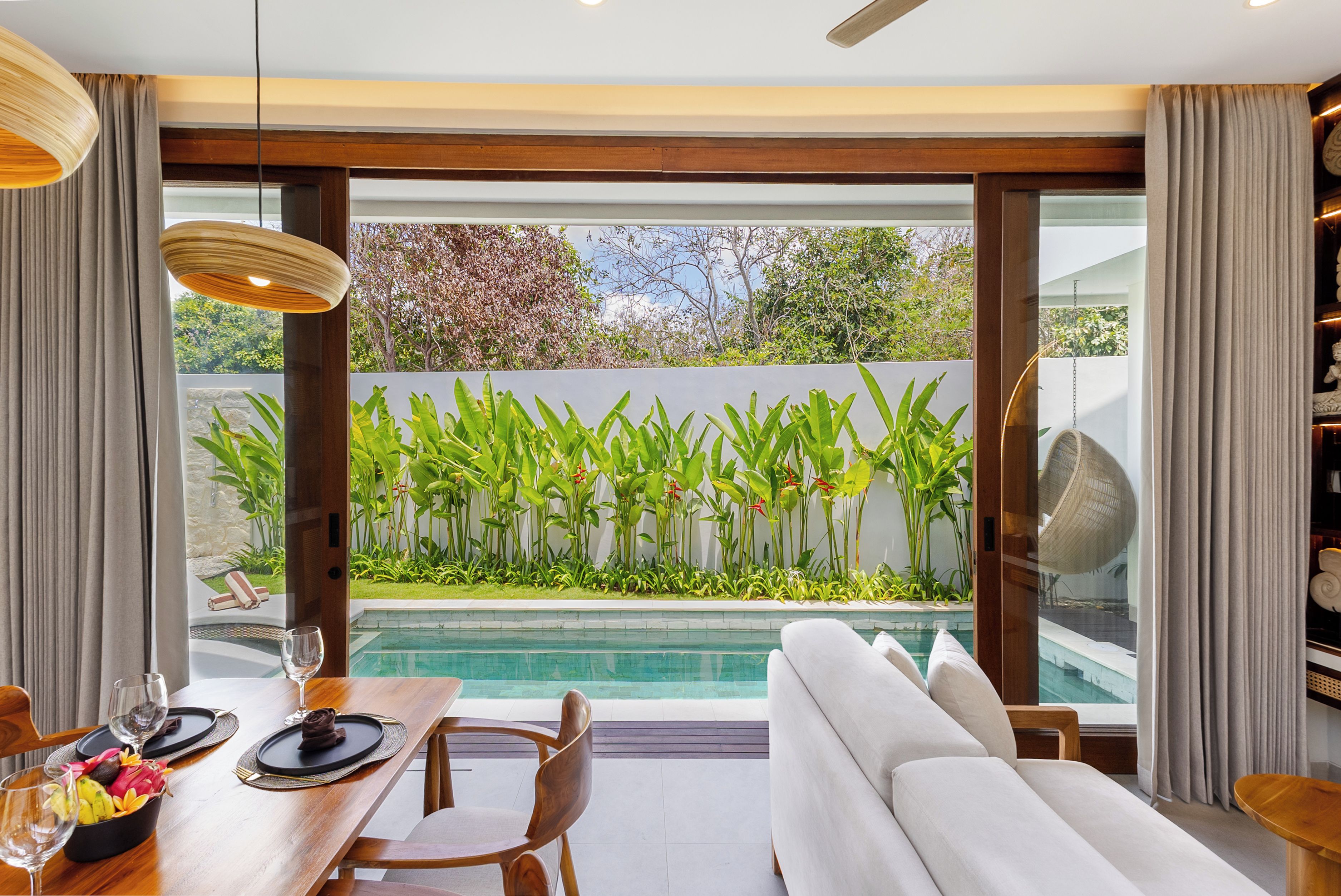 A modern interior with a dining area, a sofa, and a view of a pool and garden.