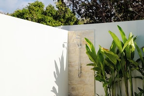 A stone shower wall with a handheld showerhead, surrounded by lush green foliage. - Niscaya Villa Uluwatu by Pertama Stay (Badung)