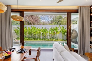 Un interior moderno con comedor, sofá y vistas a una piscina y jardín.