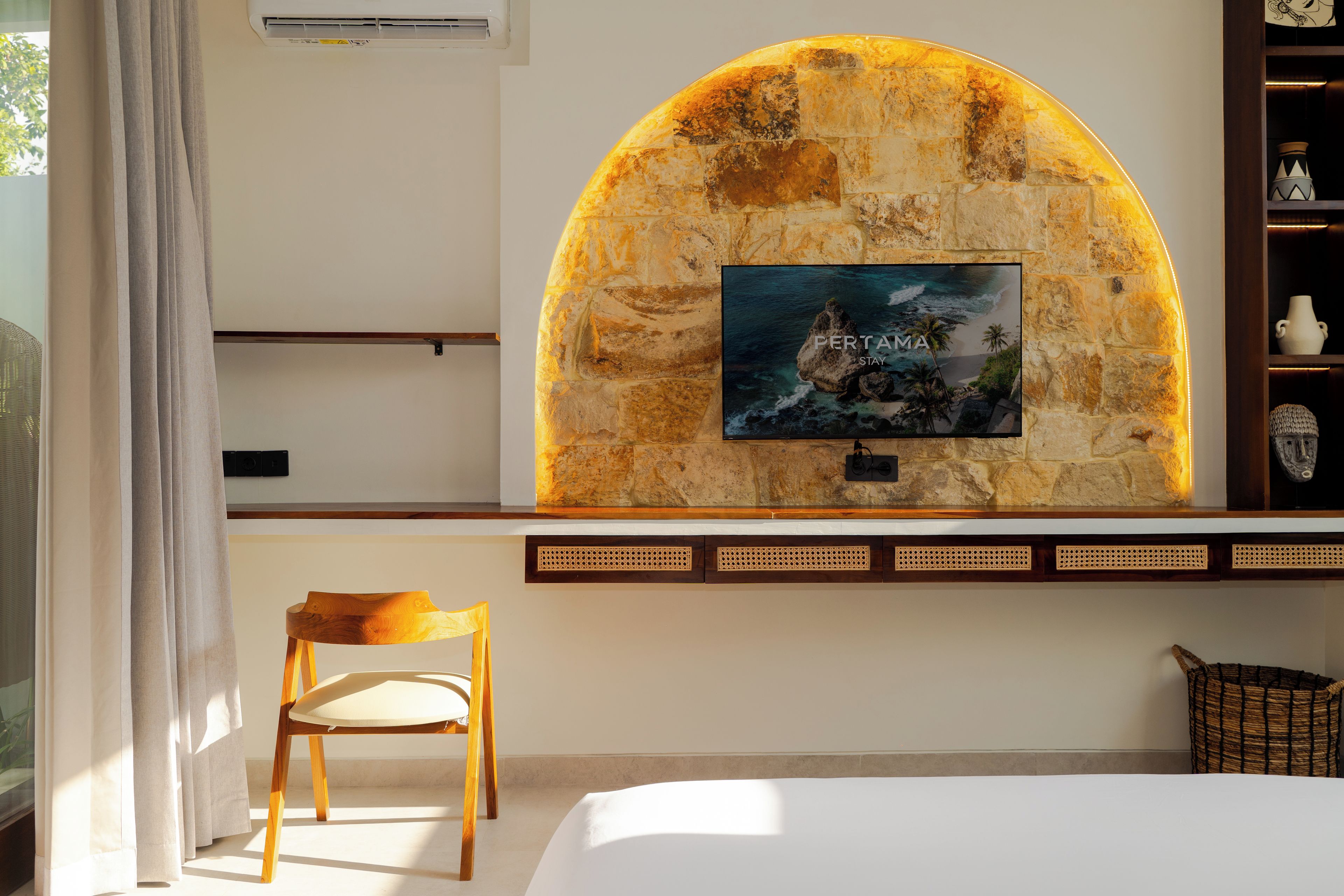 A room with a stone wall, a mounted television, a wooden chair, and a bed.