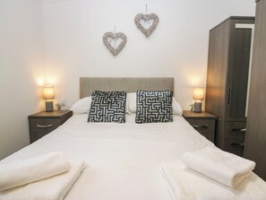 A hotel room with a bed, two heart-shaped wall decorations, two patterned pillows, two bedside lamps, a wooden wardrobe, and two folded towels. - Terabithia Lodge (Windermere)