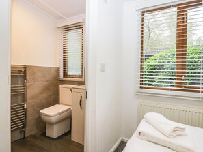 A compact bathroom with a toilet, a small cabinet, a towel rack, and a window with blinds. - Terabithia Lodge (Windermere)