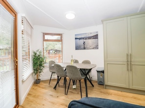 A room with a dining table, chairs, a potted plant, a painting, and a wardrobe. - Terabithia Lodge (Windermere)