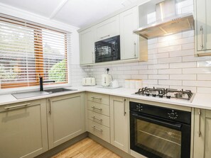 A modern kitchen with white cabinetry, a gas stove, an oven, and a window with blinds. - Terabithia Lodge (Windermere)