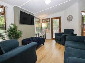 A living room with a flat-screen TV mounted on the wall, a dark blue sofa, and a wooden floor. - Terabithia Lodge (Windermere)