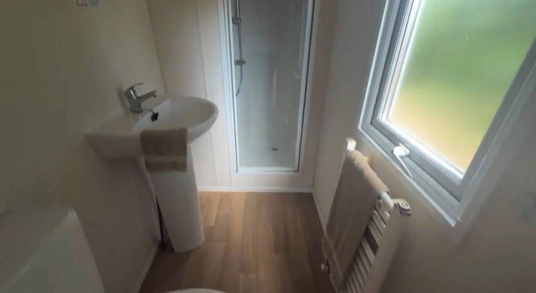 Une petite salle de bain avec un lavabo, une serviette, une douche et une fenêtre.