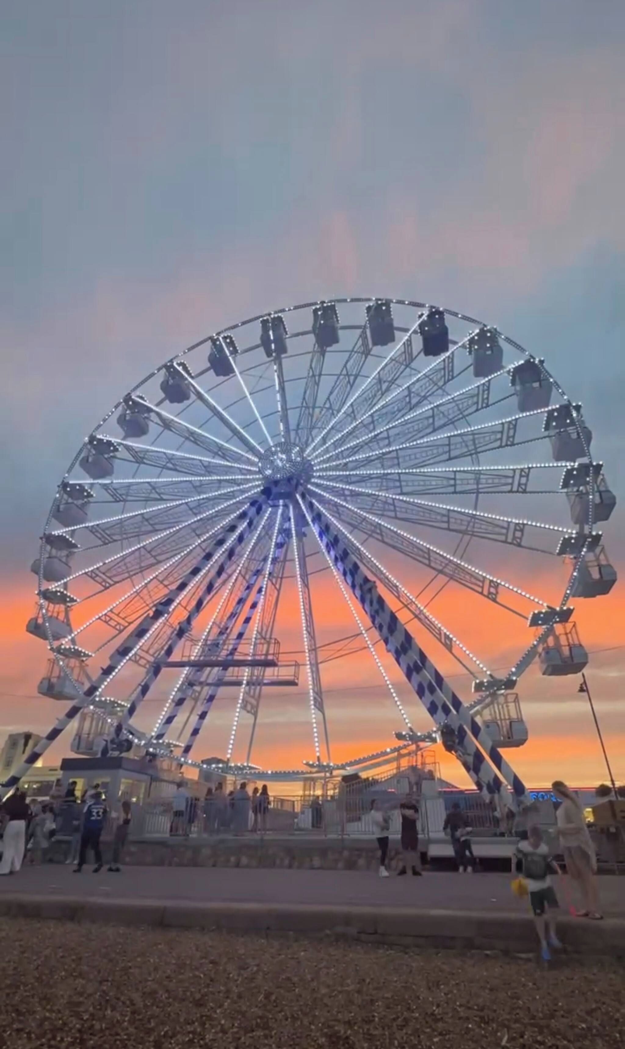 Une grande roue avec des cabines, une plateforme et une foule de personnes rassemblées autour.