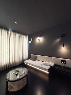 A modern hotel room with a sofa, a round coffee table, and a wall-mounted light fixture.