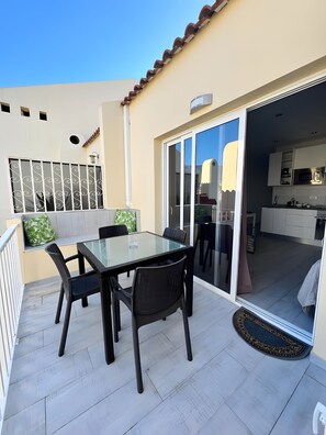 A glass-top table with four chairs on a balcony with a sliding glass door leading to a kitchen. - Vacation Apartment 'Precioso Mareverde' with Shared Pool, Wi-Fi and Air Conditioning (Costa Adeje)