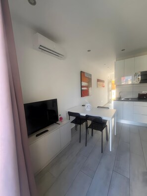 A modern living room with a flat-screen TV, a dining area with a white table and black chairs, and a kitchen with white cabinets and a microwave. - Vacation Apartment 'Precioso Mareverde' with Shared Pool, Wi-Fi and Air Conditioning (Costa Adeje)
