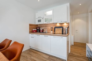 A compact kitchen with white cabinets, a wooden countertop, and a dining area with brown chairs. - Baltrum Vacation Rental (Norden)