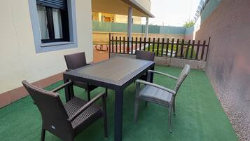 Un'area patio esterna con tavolo e sedie, una finestra e un pavimento in prato sintetico verde.