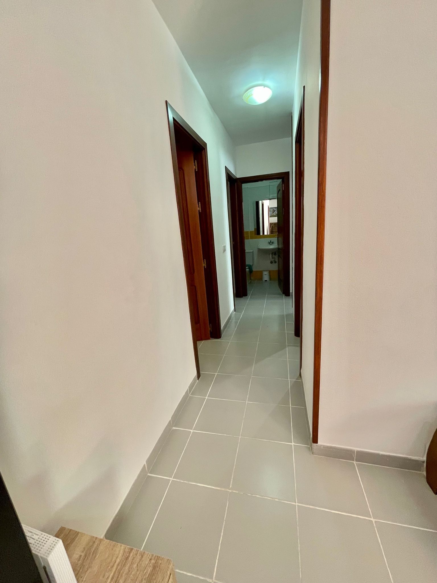 Ein Korridor mit gefliestem Boden, der zu einem Badezimmer mit Waschbecken und Toilette führt.