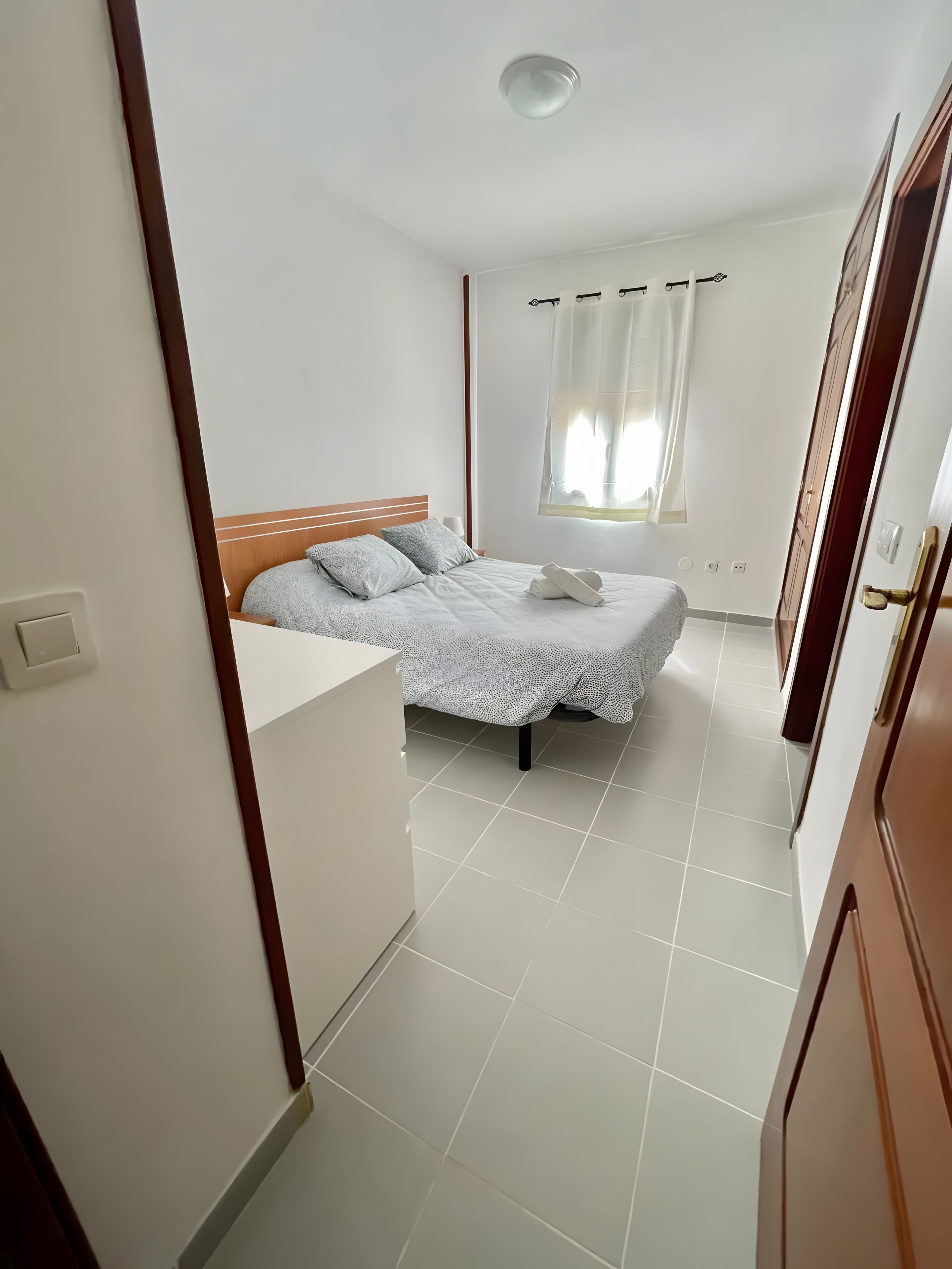 Una camera da letto con un letto, una finestra con tende e un pavimento piastrellato.