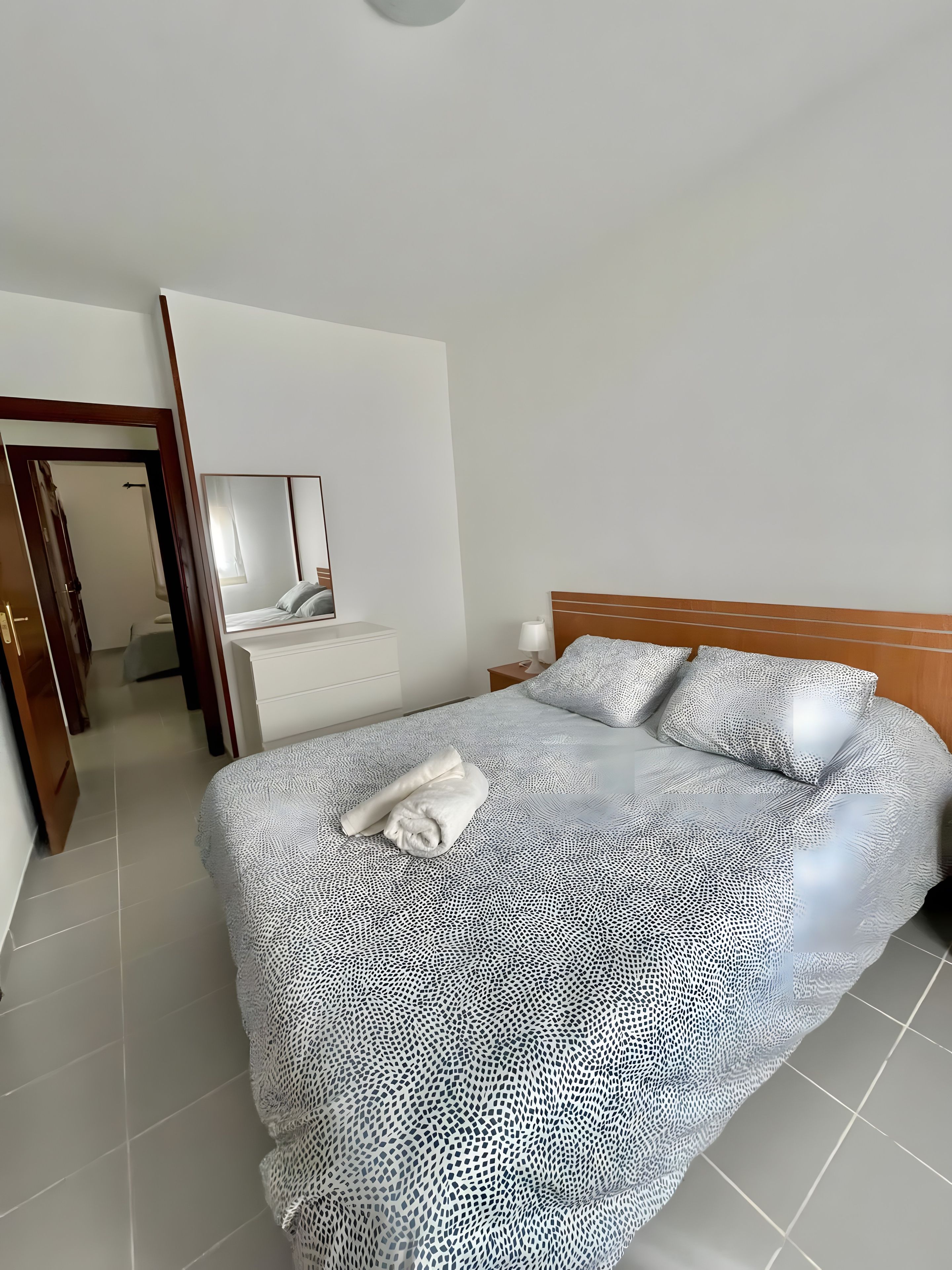 Ein Hotelzimmer mit Bett, Nachttisch, Spiegel und einer Tür zu einem anderen Raum.