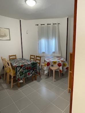 Zona pranzo con tavolo e sedie, una finestra con tende e una porta.