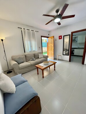Un soggiorno con un divano, un tavolino da caffè, una ventola a soffitto e vista sulla cucina.