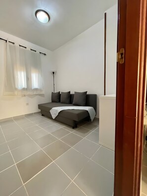Ett rum med en soffa, en vit vägg, en taklampa och en dörr.