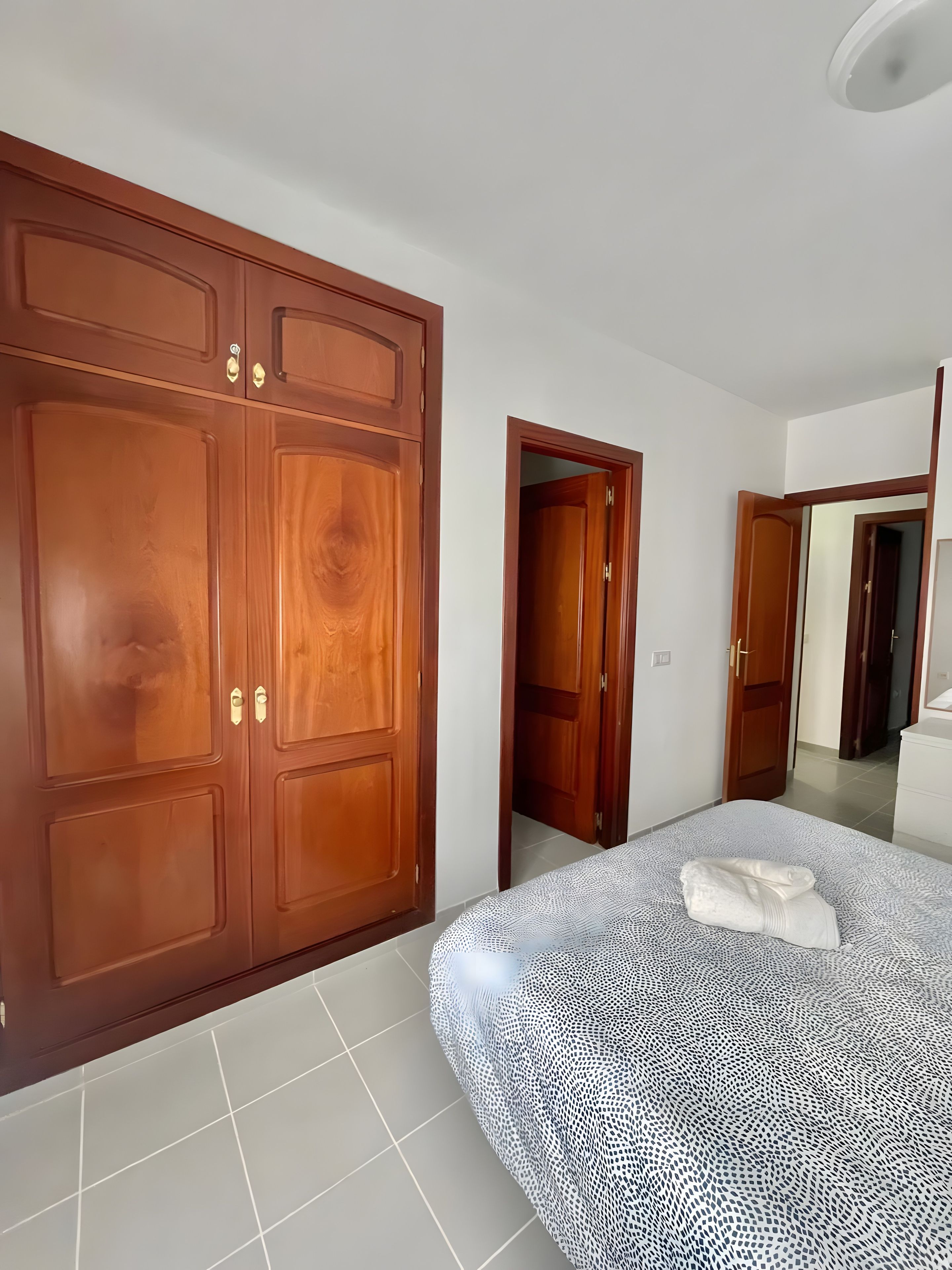 Een slaapkamer met een grote garderobe, een bed met een beddengoed met een patroon, en een betegelde vloer.