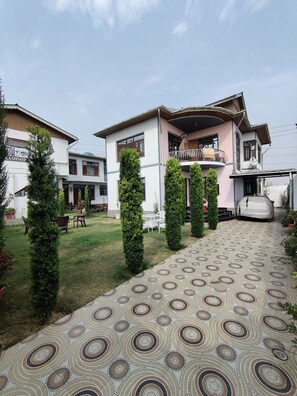 A two-story house with a balcony, a patterned driveway, and a small garden with chairs and potted plants. - KASHMIR HOMESTAY (Baramula)