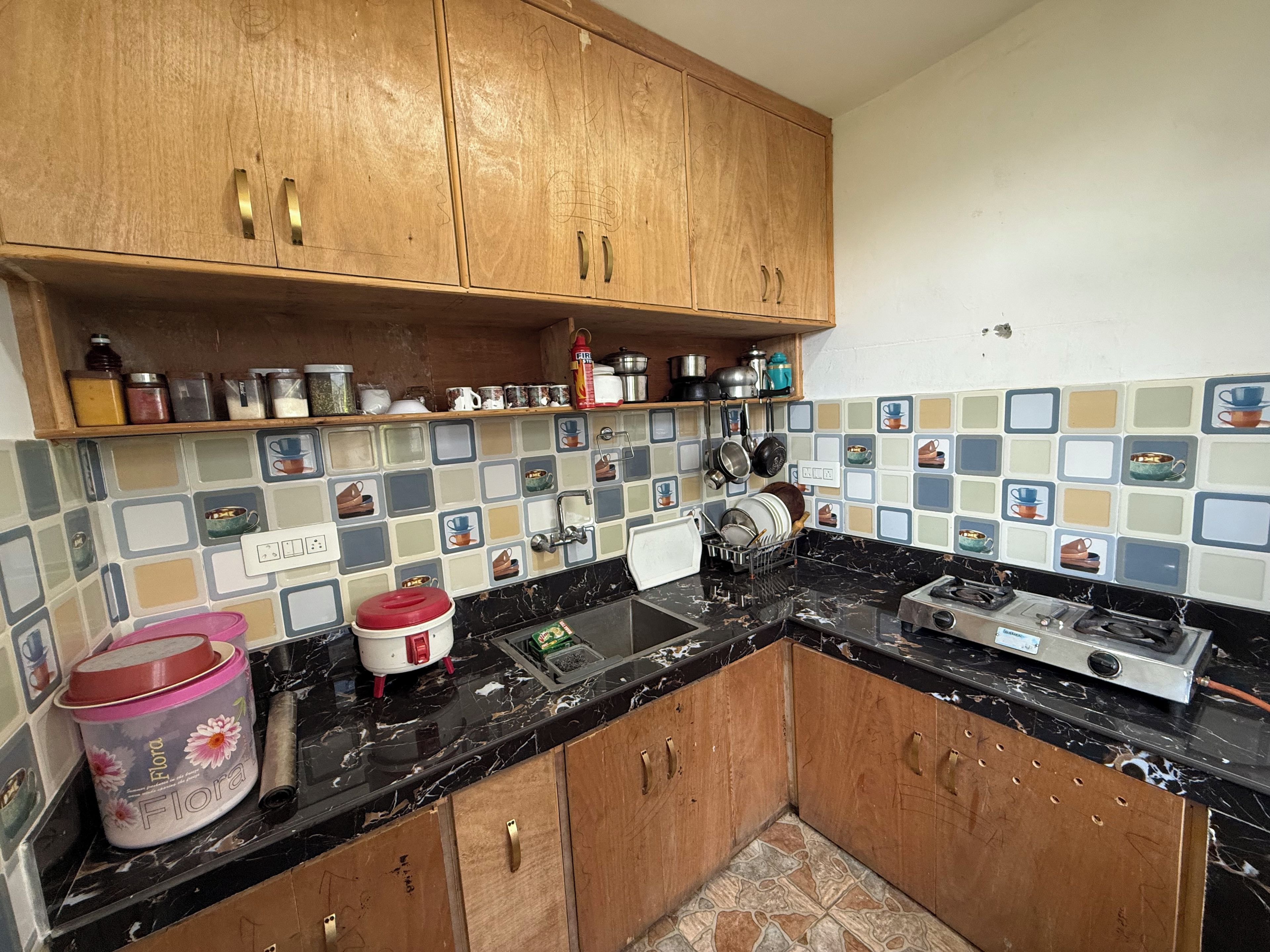 Una cocina con armarios de madera, encimera negra y salpicadero de azulejos con diseños de tazas.