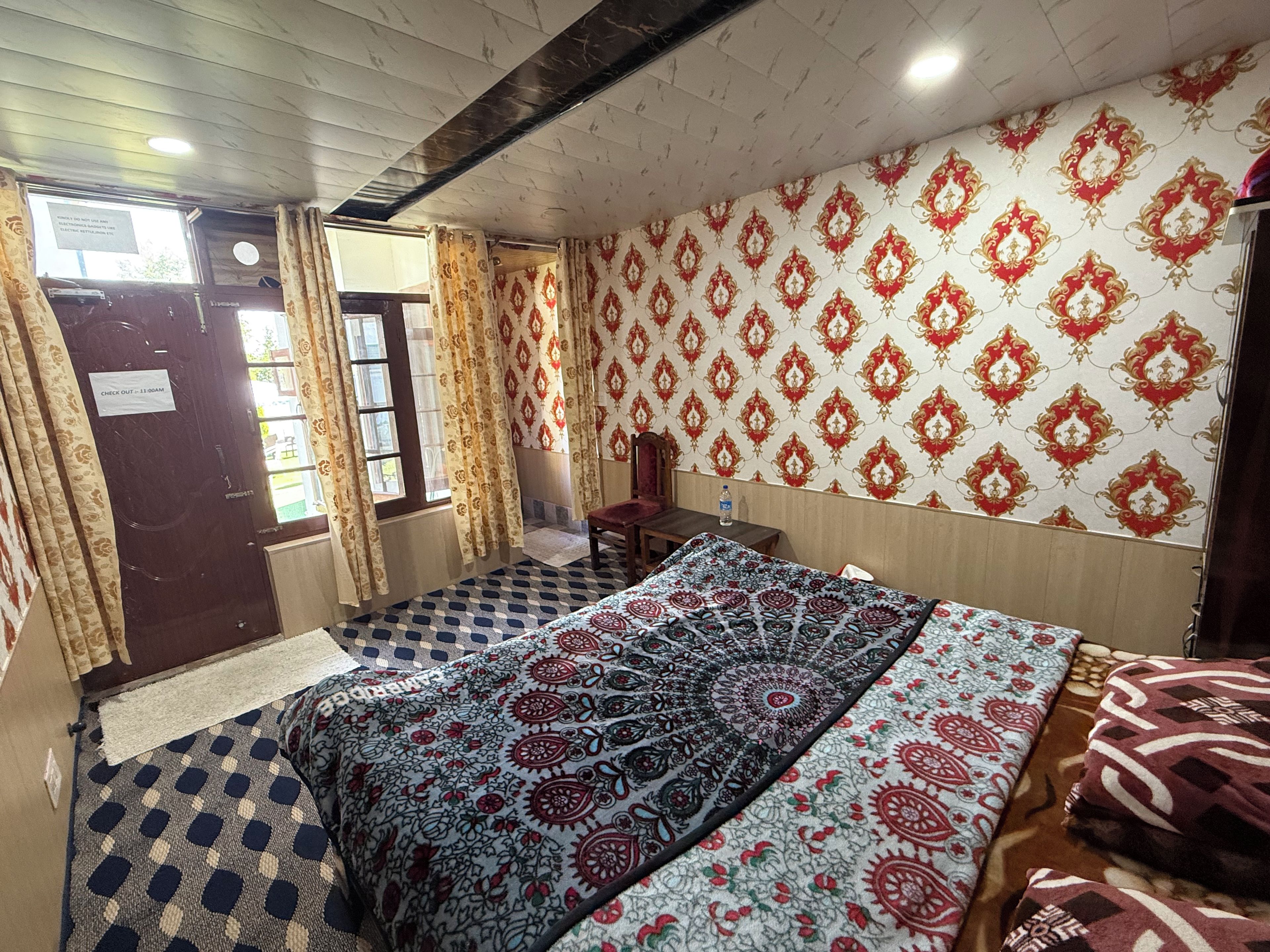 Una habitación con un cartel de recepción, una cama con ropa de cama estampada, una silla, una mesa y una pared con diseño.
