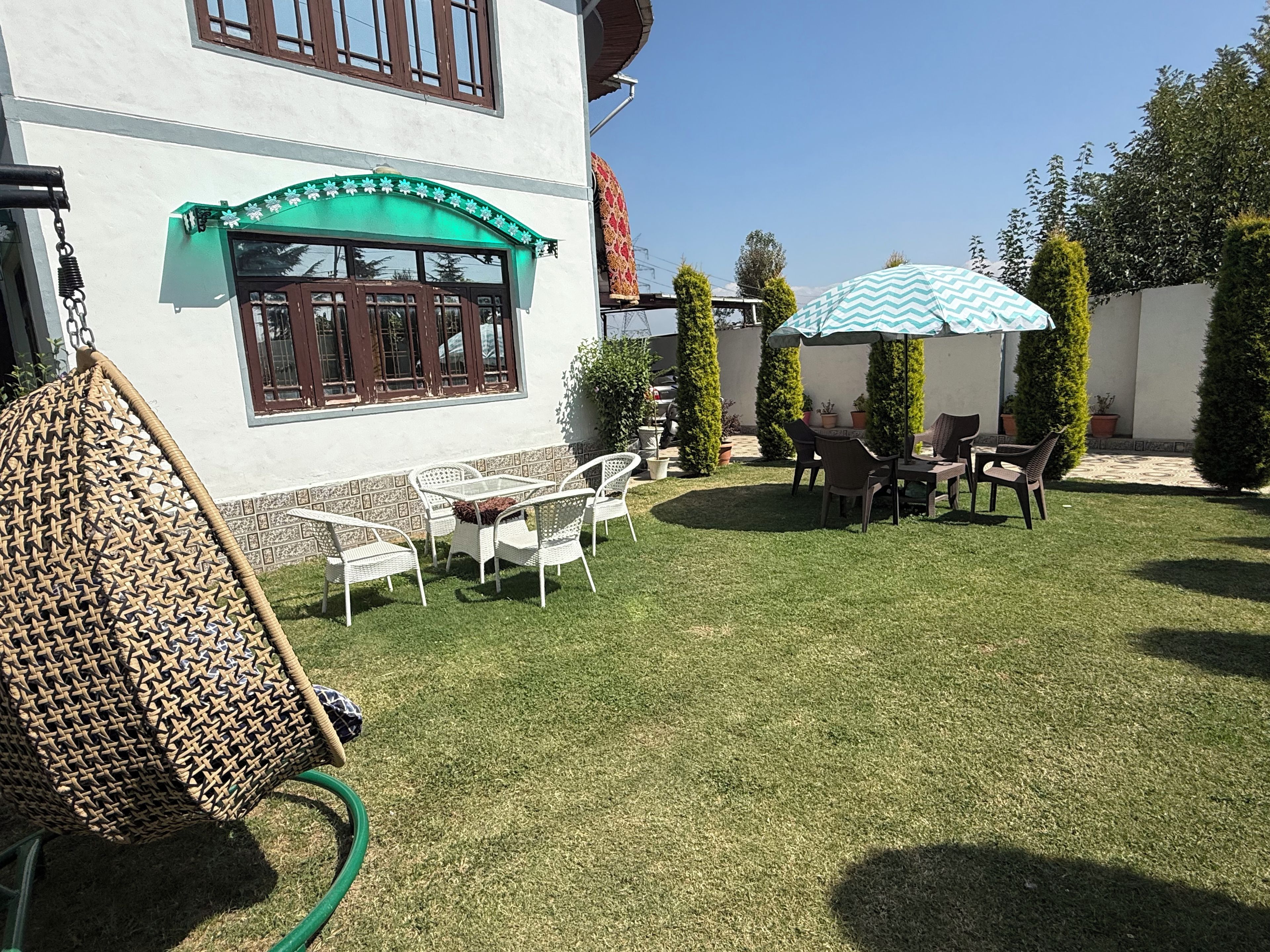 Un patio con mobiliario exterior, una sombrilla verde y un edificio blanco con un arco decorativo.