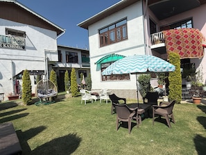 A courtyard with outdoor seating, a hanging chair, and a building with a sign reading 'E KASHMIR'. - KASHMIR HOMESTAY (Baramula)
