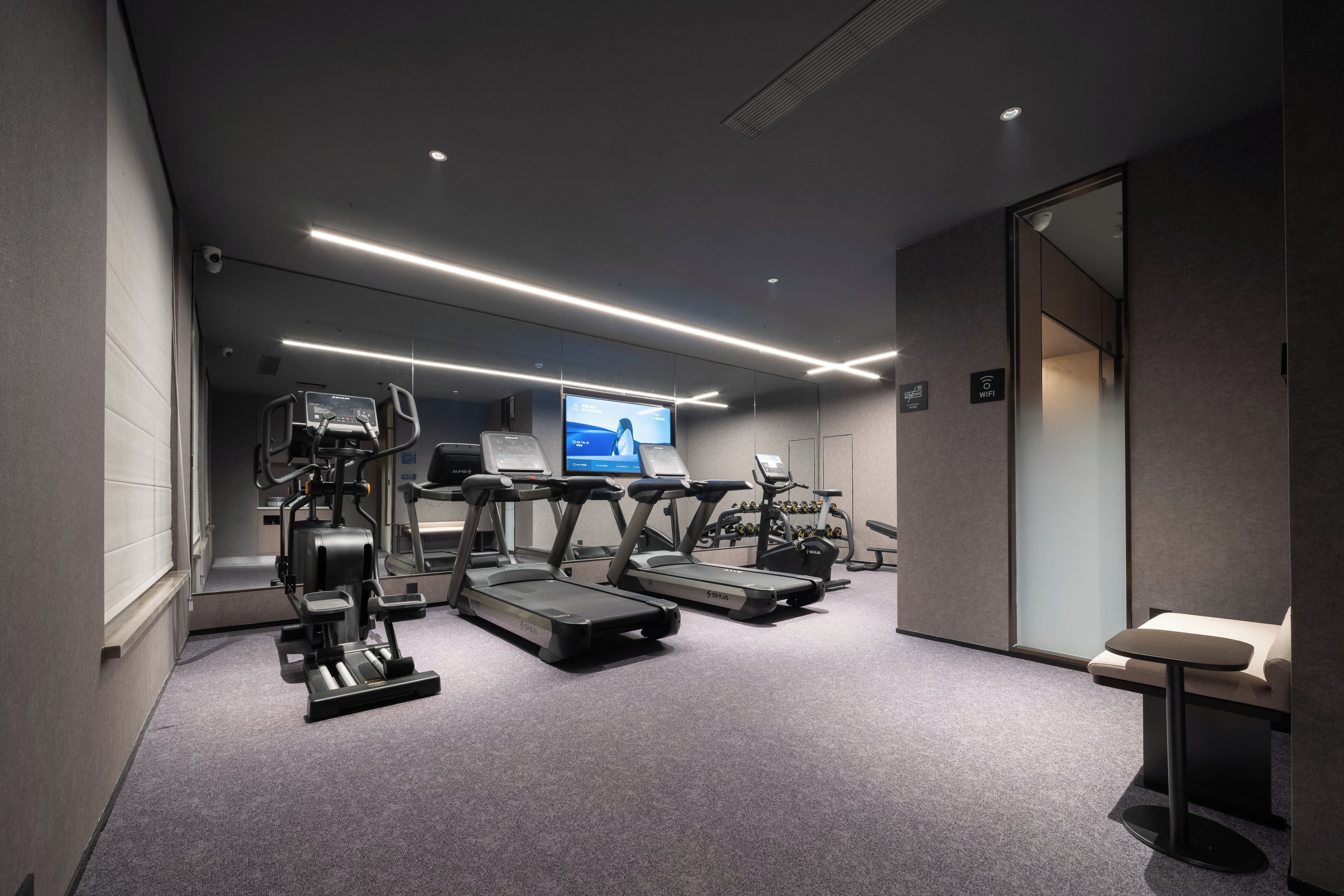 Un gimnasio moderno con cintas de correr, elípticas y una pantalla de televisión mostrando información sobre ejercicios.