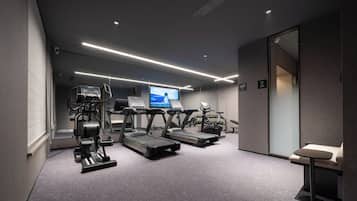 Un gimnasio moderno con cintas de correr, elípticas y una pantalla de televisión mostrando información sobre ejercicios.