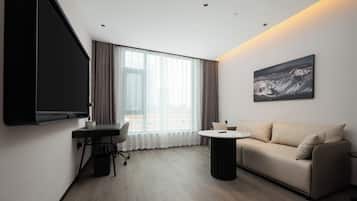 Una habitación de hotel moderna con televisión de pantalla plana, un sofá, una mesita redonda y un amplio ventanal con cortinas.