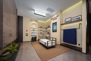 Habitación de hotel con cama, un pequeño escritorio, repisa con objetos, televisor montado en la pared y un perchero.