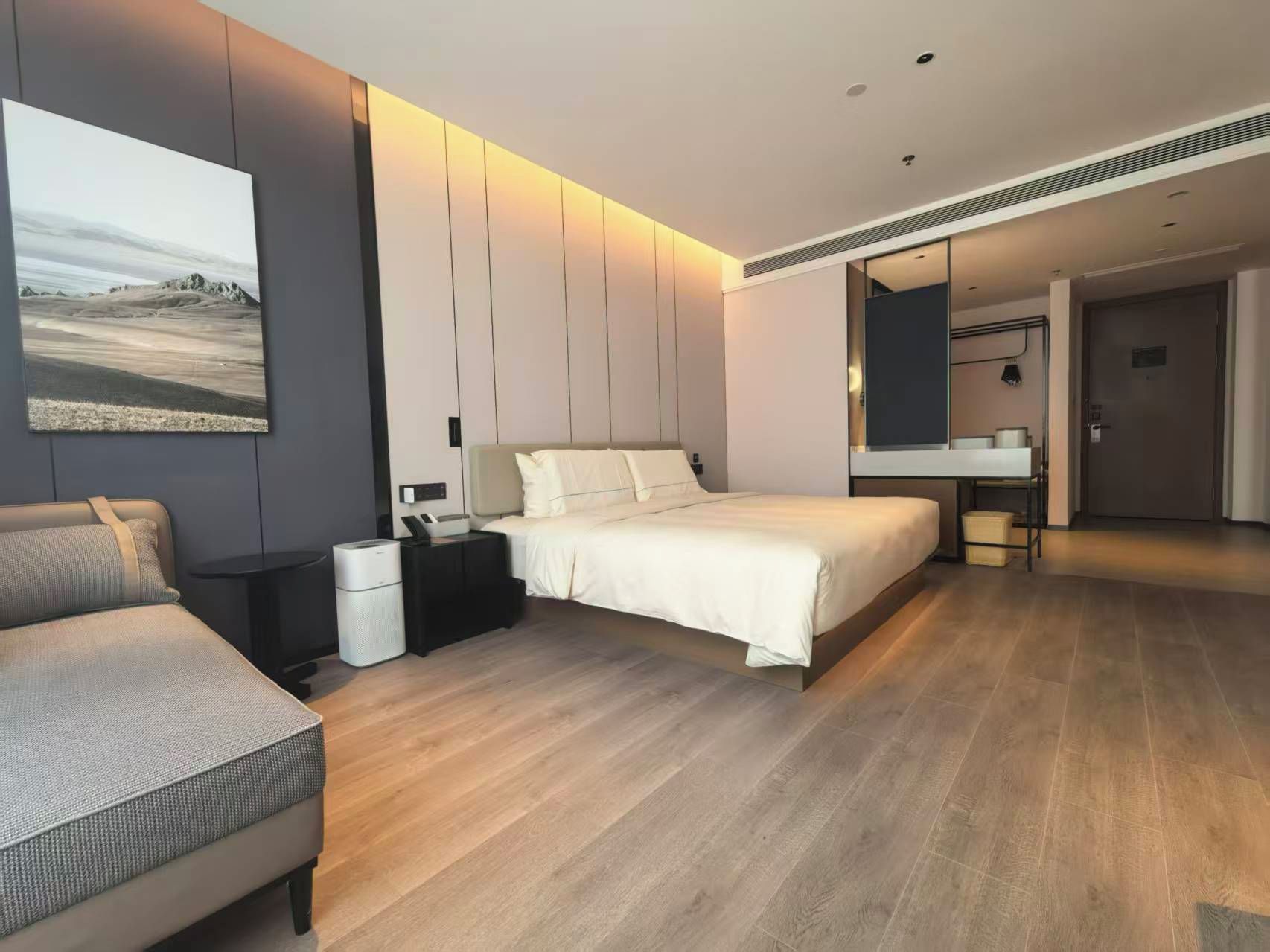A modern hotel room with a large bed, bedside tables, a desk, and a bathroom visible through an open door.