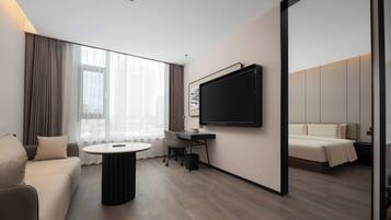 A modern hotel room with a sofa, a small round table, a desk, a television, and a large mirror.
