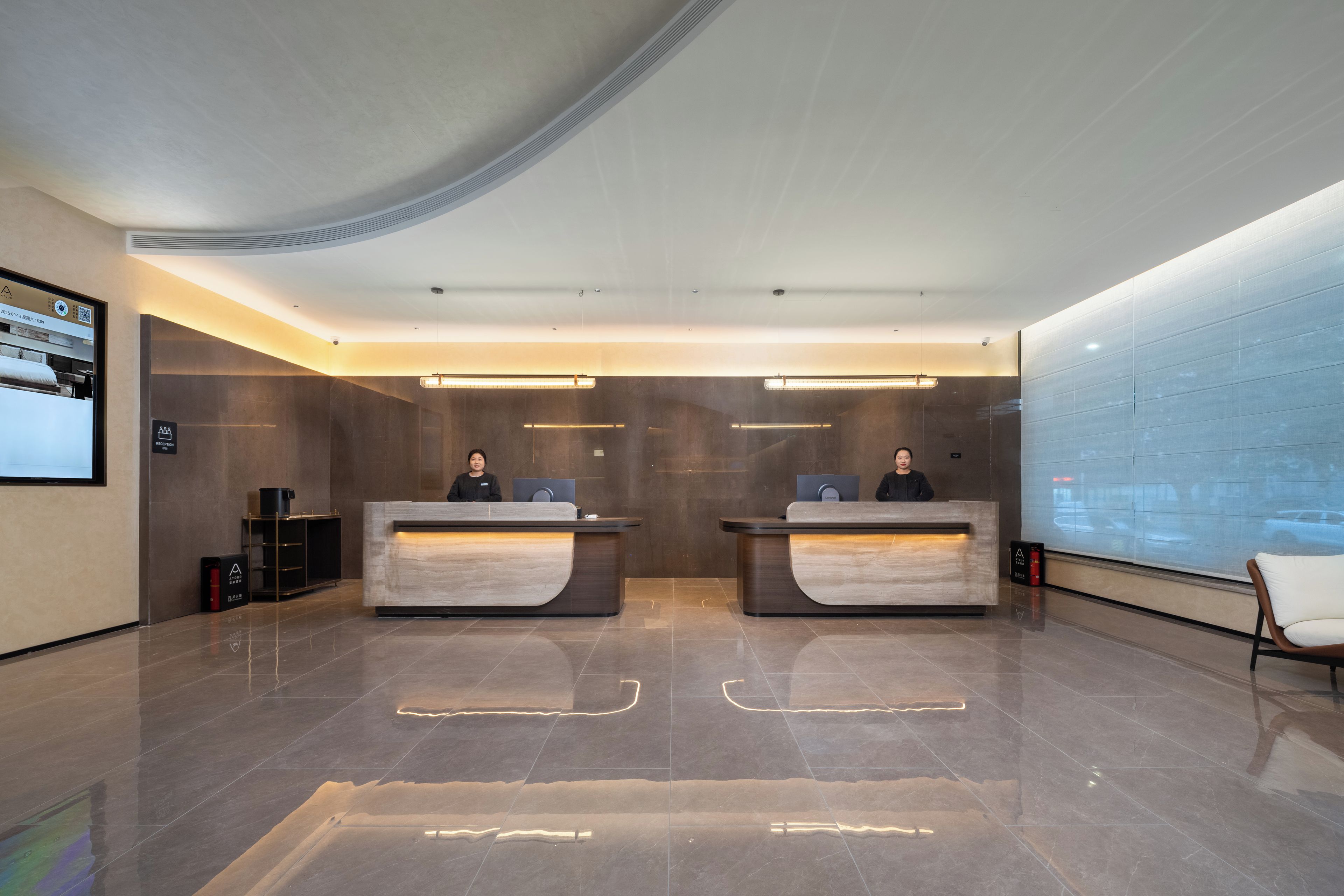 Un área de recepción moderna con dos mostradores, una pantalla digital y un muro de cristal.