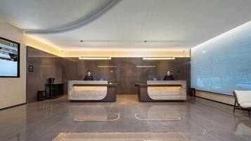 Un área de recepción moderna con dos mostradores, una pantalla digital y un muro de cristal.