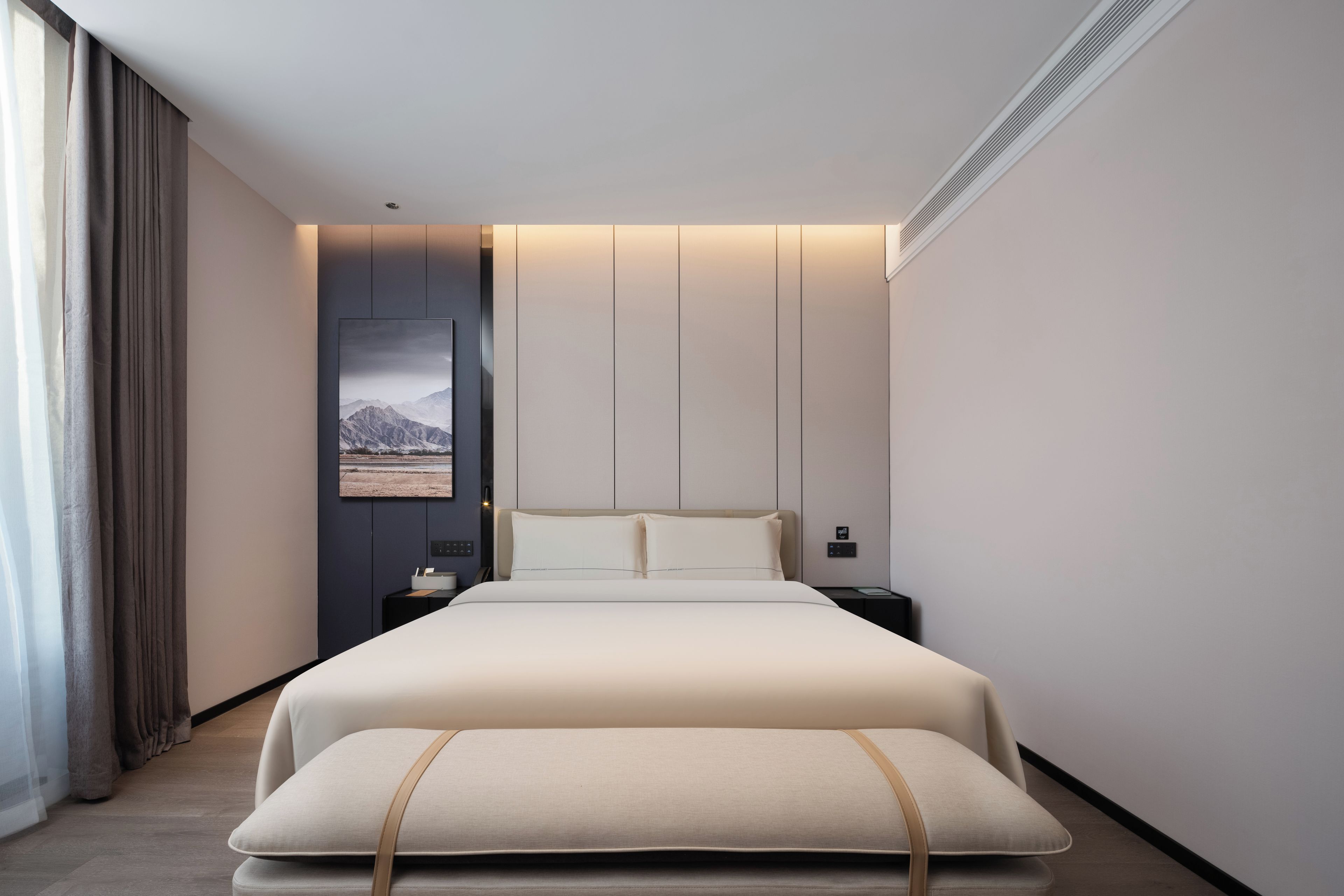 A modern hotel room with a large bed, bedside tables, a nightstand, a bench, and a view of mountains through the window.