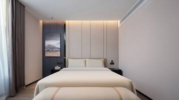 A modern hotel room with a large bed, bedside tables, a nightstand, a bench, and a view of mountains through the window.