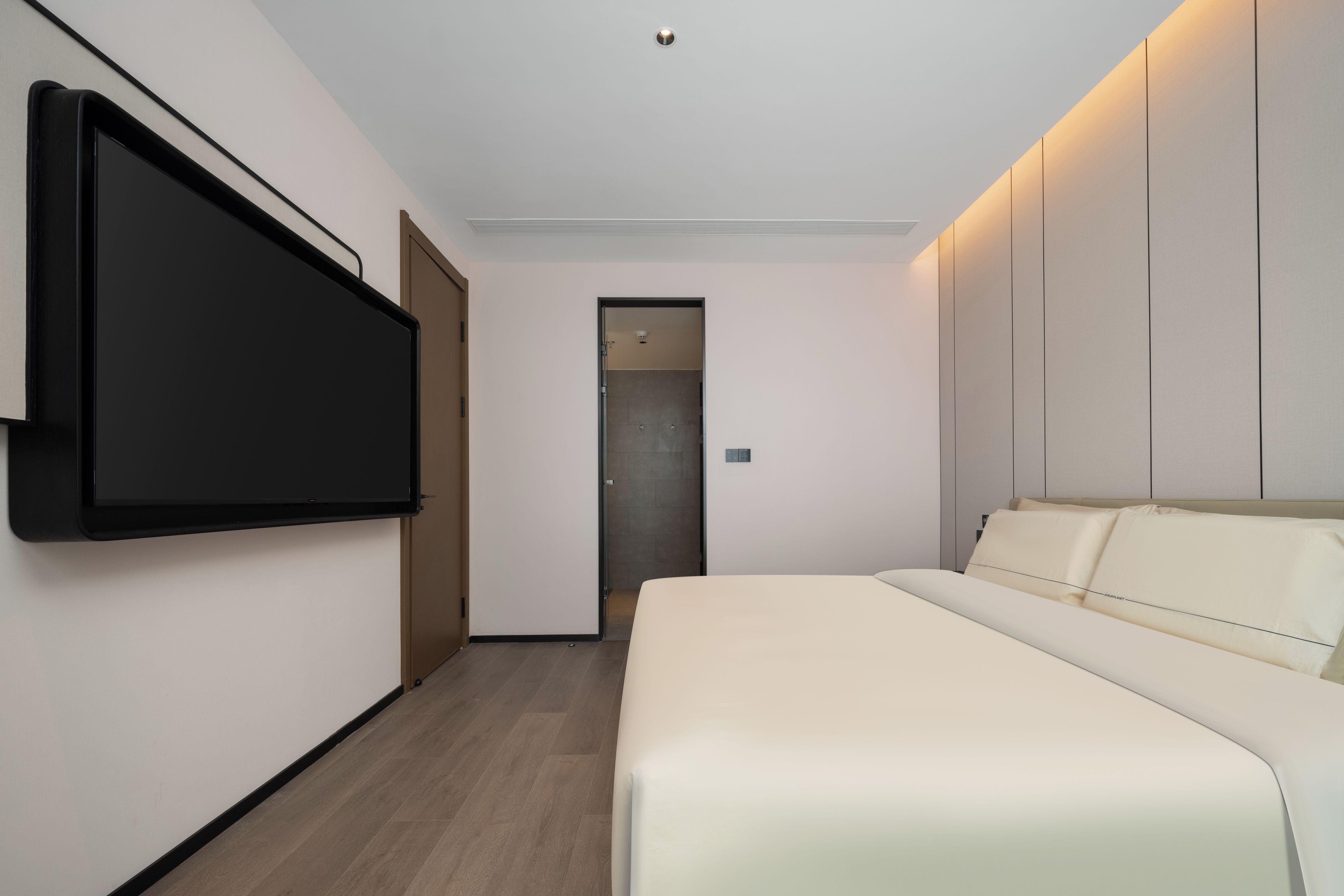Habitación de hotel moderna con una televisión de pantalla plana grande montada en la pared, una cama con cabecera y una puerta que da a un baño.