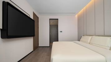 Habitación de hotel moderna con una televisión de pantalla plana grande montada en la pared, una cama con cabecera y una puerta que da a un baño.