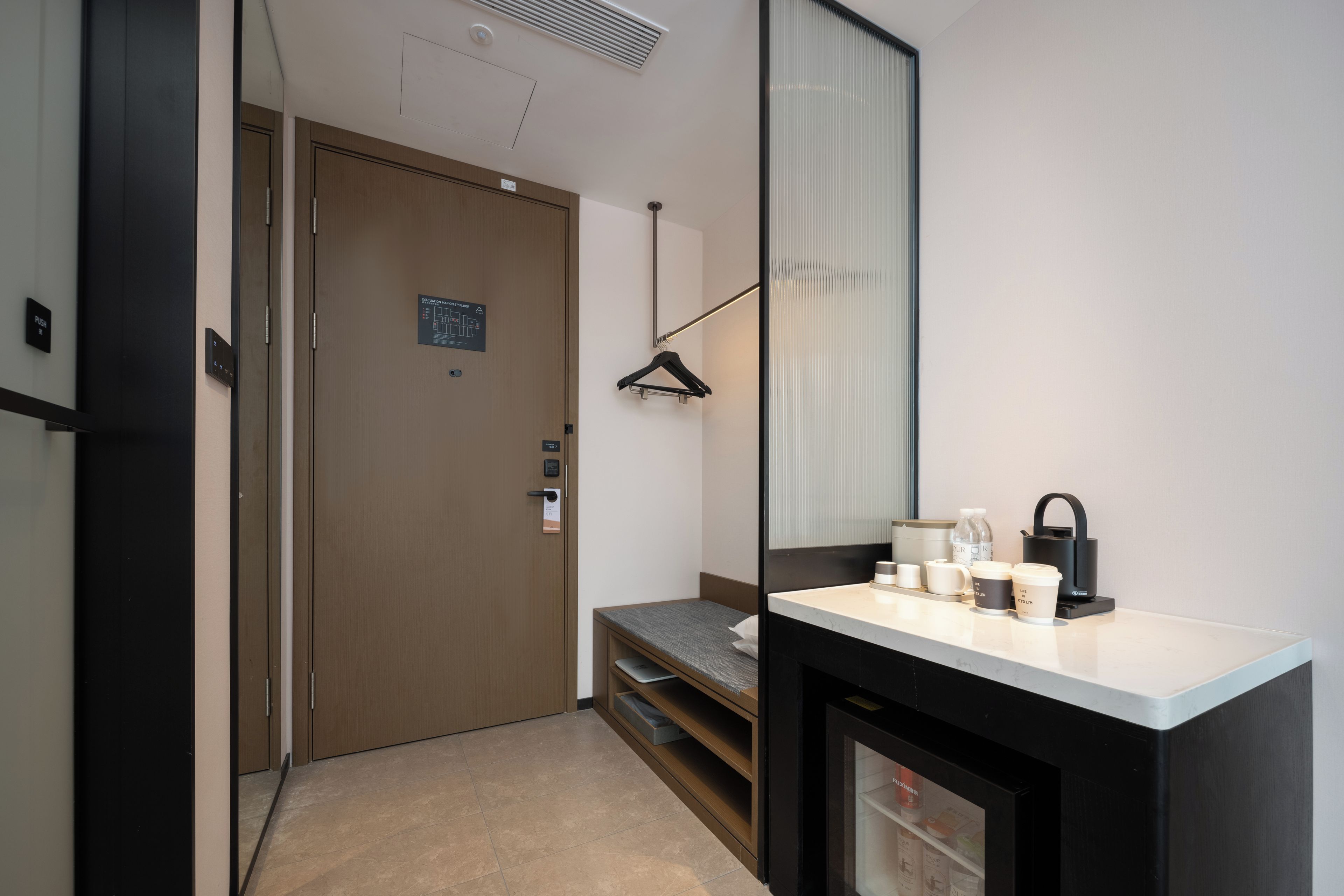 A hotel room with a bed, a bedside table, a mirror, a hanging coat rack, and a small kitchenette area.