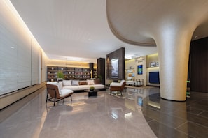 Een ruime lobby met een moderne bank, een salontafel en een boekenkast vol boeken.