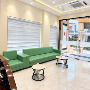 Un área de recepción con un sofá verde, dos mesas redondas y una puerta de vidrio que da al exterior.
