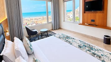 Habitación de hotel con una cama grande, un televisor en la pared, una mesita y vistas a la playa.