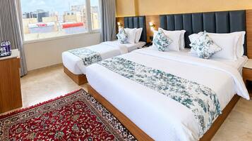 A hotel room with two beds, a large window, a ceiling fan, and a red patterned rug.