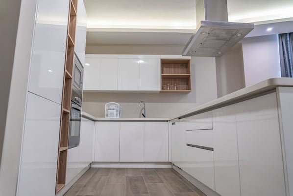 A modern kitchen with white cabinetry, a built-in microwave, and a stainless steel range hood. - Rapenda 2bedroom Park View Apartments (Nairobi)