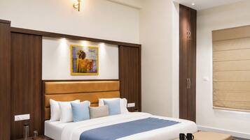 A hotel room with a bed, bedside tables, a nightstand, a wall-mounted artwork, a window with blinds, and a wardrobe.