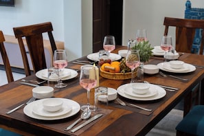 A dining table set with plates, glasses, cutlery, and a fruit basket. - Alaya Stays Riva Amar Villa 3BHK (Udaipur)